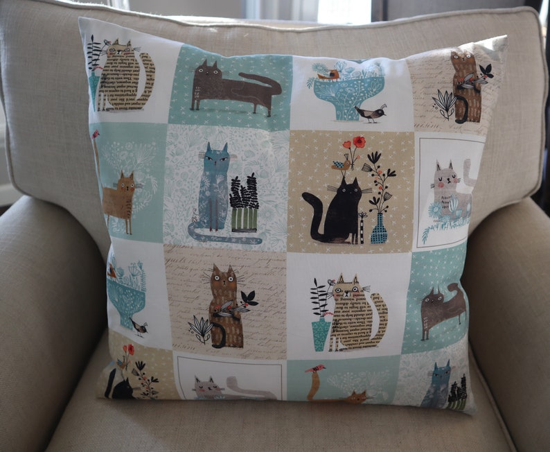 Pu&ograve; includere: Un cuscino decorativo con un design a patchwork che presenta diverse illustrazioni di gatti in varie pose e colori. Lo sfondo &egrave; una miscela di blu chiaro, beige e bianco.