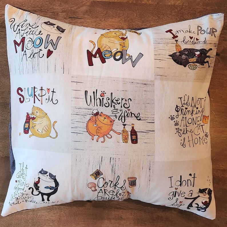 Pu&ograve; includere: Un cuscino beige e marrone con un design a patchwork che presenta gatti e giochi di parole sul vino. Il cuscino ha una variet&agrave; di detti tra cui "Wine a little meow alot", "Slurp it", "Whiskers are fine", "It's not drinking alone if the cat is home", "Corks are for dust", e "I don't give a sip".