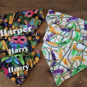 May include: Three colorful dog bandanas with Mardi Gras themed fabric. The bandanas are black with gold and green accents and feature a purple, green, and gold beaded pattern. The bandanas are personalized with the names "Harper", "Harry", and "Henry".