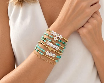 Può includere: Una serie di sei braccialetti con perline turchesi, perline metalliche dorate e perline bianche con lettere che compongono MAMA, ELLA e BEN. Il set include un ciondolo a cuore dorato, una sottile barretta dorata e una delicata catenina a cuori.