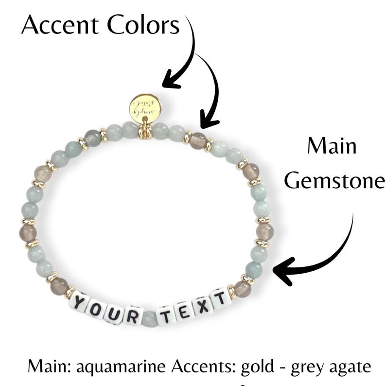 May include: A beaded bracelet featuring aquamarine and grey agate stones, with gold accents. The bracelet includes white letter beads spelling "YOUR TEXT". A small gold charm is attached. The main gemstone is aquamarine.
