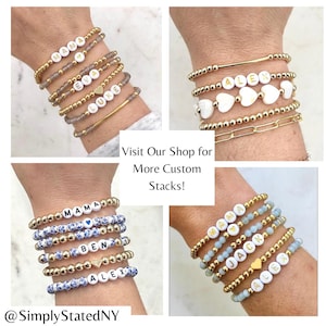 May include: Four stacks of beaded bracelets featuring gold-tone metallic beads, white letter beads spelling names like MAMA, EVA, LUKE, ALEX, BEN, and JACK, and heart-shaped beads. Some bracelets include blue floral or light blue glass beads.