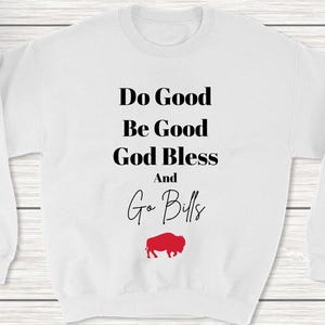 Puede incluir: Sudadera blanca con texto negro que dice "Do Good Be Good God Bless And Go Bills" con una silueta de búfalo roja debajo del texto.