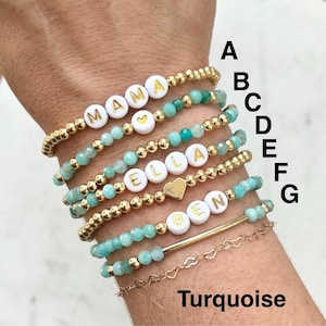 Stacked stretch beaded bracelets with gold-tone and pale-blue beads; white alphabet beads spell names for a personalized kids name bracelet set.