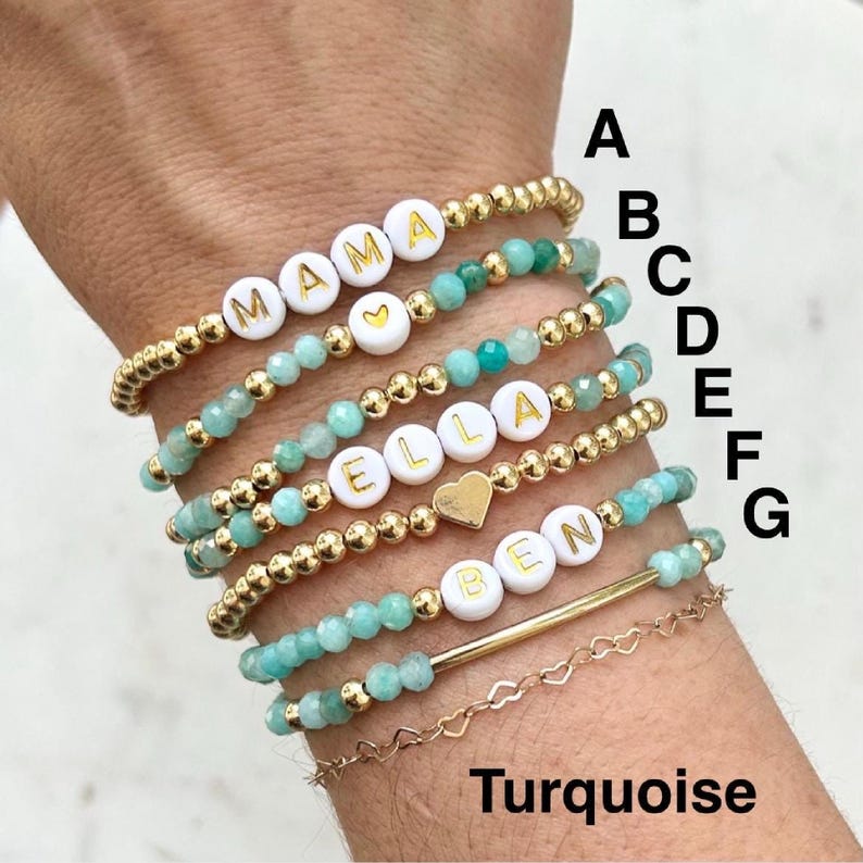 Stacked stretch beaded bracelets with gold-tone and pale-blue beads; white alphabet beads spell names for a personalized kids name bracelet set.
