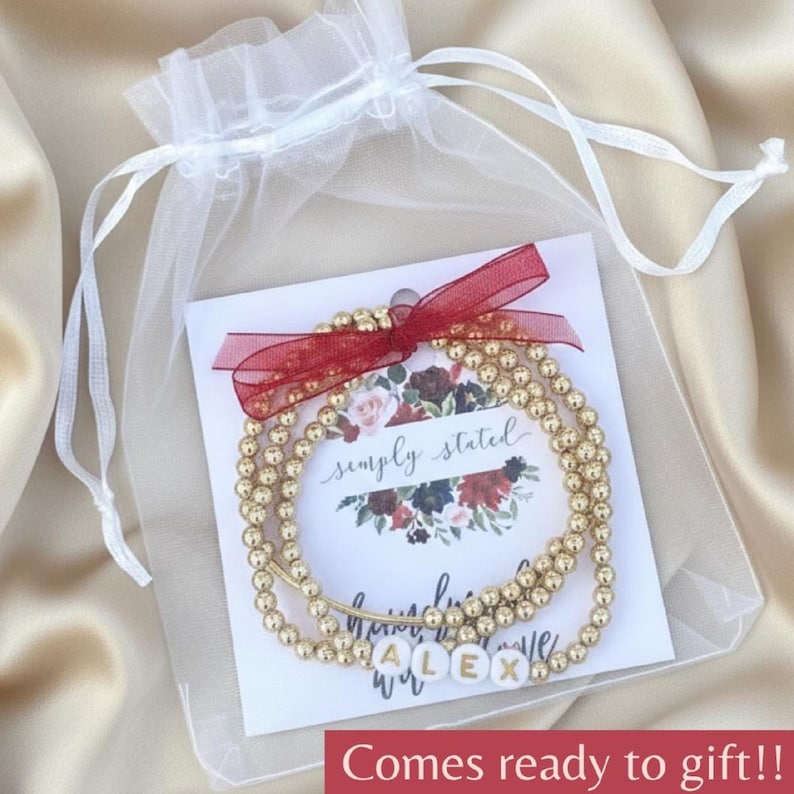 Stacked stretch beaded bracelets with gold-tone and pale-blue beads; white alphabet beads spell names for a personalized kids name bracelet set.