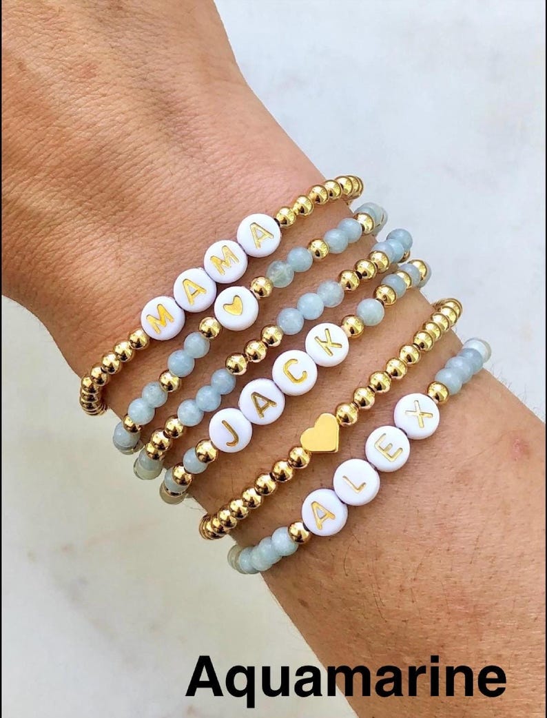 Stacked stretch beaded bracelets with gold-tone and pale-blue beads; white alphabet beads spell names for a personalized kids name bracelet set.