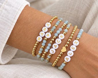Può includere: Un set di cinque braccialetti elastici con un mix di perline metalliche dorate, perline in pietra azzurra e perline circolari bianche con lettere dorate. I braccialetti riportano le parole MAMA, JACK e ALEX, insieme a ciondoli a cuore dorati.