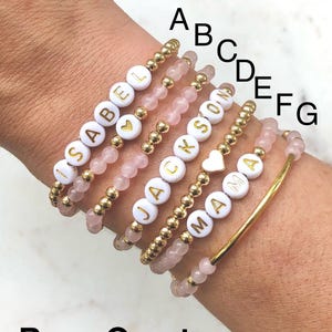 Stacked stretch beaded bracelets with gold-tone and pale-blue beads; white alphabet beads spell names for a personalized kids name bracelet set.