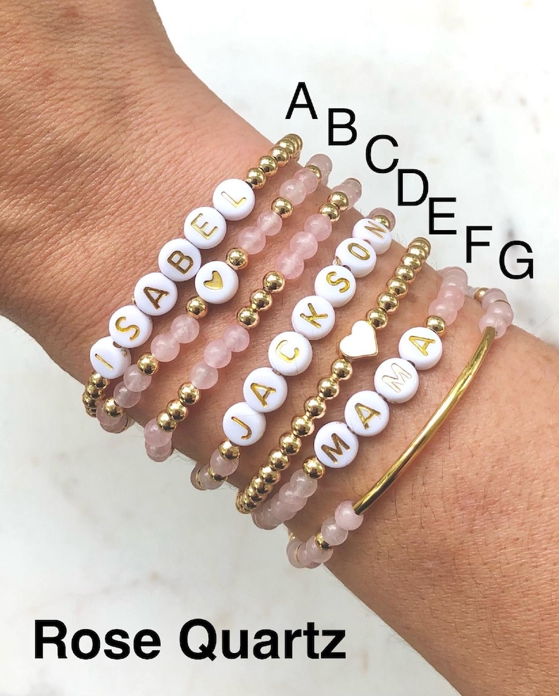 Stacked stretch beaded bracelets with gold-tone and pale-blue beads; white alphabet beads spell names for a personalized kids name bracelet set.