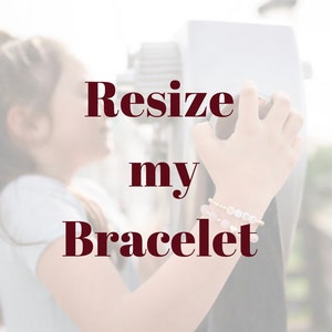 May include: Resize my Bracelet text on a blurred background with a person's hand wearing a bracelet with pink, white, and gold beads.