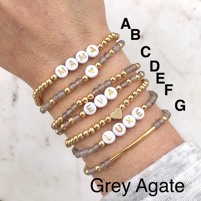 Stacked stretch beaded bracelets with gold-tone and pale-blue beads; white alphabet beads spell names for a personalized kids name bracelet set.
