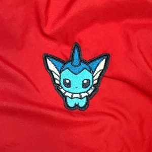 May include: A blue and white embroidered patch of a cartoon water-type Pokemon with a fin on its head and a frilly collar.