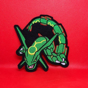 May include: Green and black embroidered patch of a Pokemon character, possibly a dragon or lizard, with a yellow ring around its neck. The character is curled up in a defensive position with its claws out.
