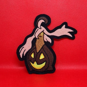 May include: A pink and brown embroidered patch of a ghost wearing a jack-o'-lantern costume.