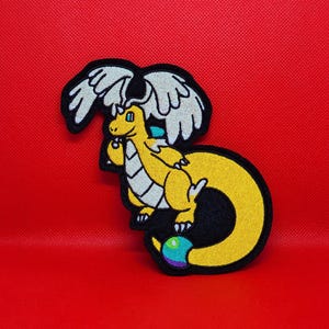 May include: A yellow dragon patch with white wings and a black outline, set against a red background. The dragon has a curved tail and a multi-colored orb at the end. The patch is likely for clothing or accessories.
