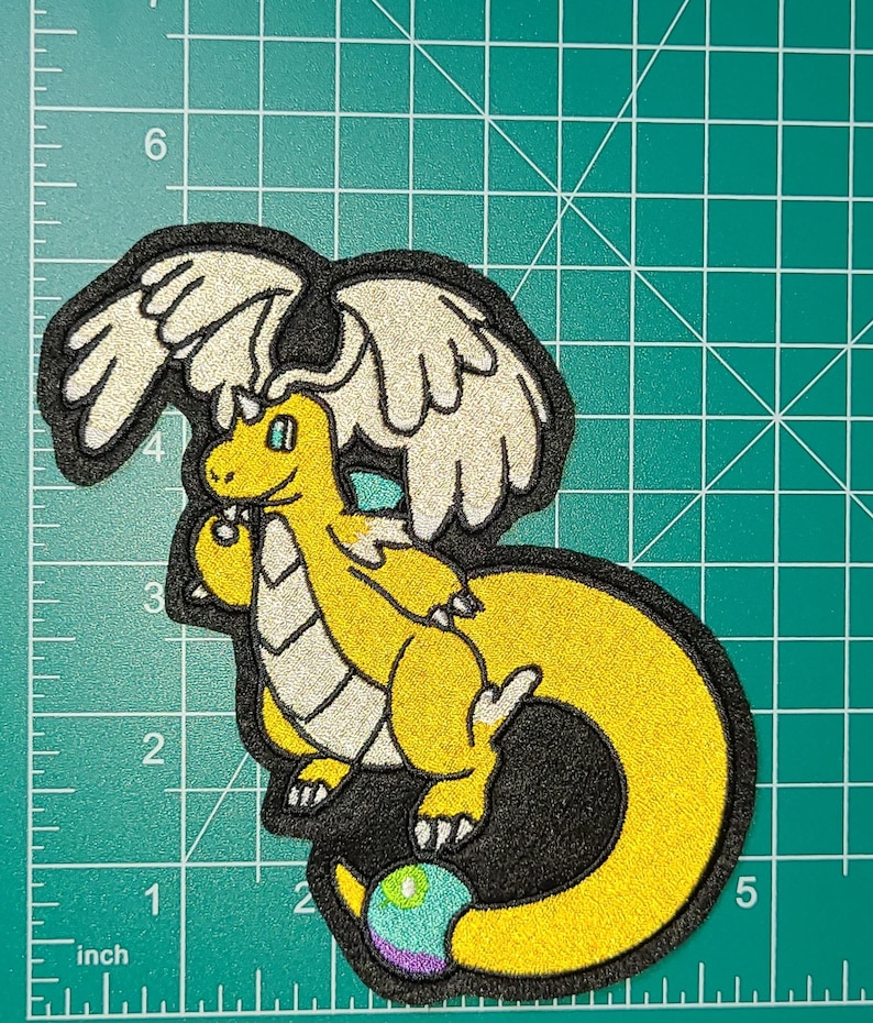 Peut inclure: &Eacute;cusson brod&eacute; repr&eacute;sentant un dragon jaune avec des ailes blanches, un contour noir et un globe multicolore. L'&eacute;cusson mesure environ 10 cm de haut et 13 cm de large.