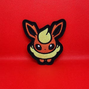 May include: Embroidered patch featuring a cartoon Flareon character with orange, yellow, and black details. The patch is on a red background. This patch is suitable for jackets, bags, or other fabric items.