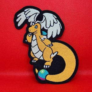 May include: An embroidered patch featuring a yellow dragon-like creature with white wings, a white belly, and a long tail ending in a blue, green, and pink sphere. The design is outlined in thick black thread against a solid red background.
