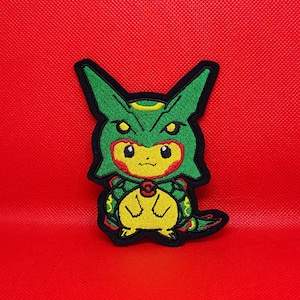 May include: Embroidered patch of a green and yellow cartoon character with a black outline, on a bright red background. The character has large eyes and a detailed design, suitable for clothing or accessories.