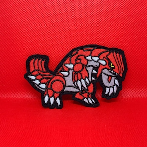 Peut inclure: Patch brodé rouge et gris d'une créature mythique avec des griffes et des dents acérées.