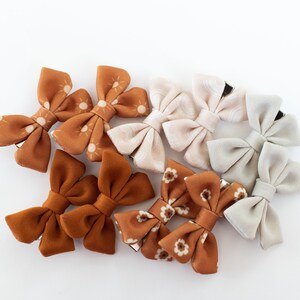 May include: A set of nine fabric hair bows in various patterns and colors. The bows are made of a soft, velvety fabric and feature a variety of designs, including sunbursts, floral prints, and solid colors. The bows are attached to alligator clips, making them easy to clip into hair.