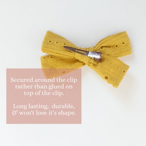 May include: A yellow fabric bow with a small metal clip. The bow is secured around the clip, rather than glued on top of it.  The text "Secured around the clip rather than glued on top of the clip. Long lasting, durable, & won't lose it's shape." is written below the bow.
