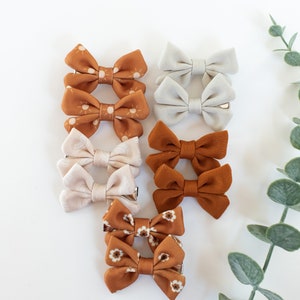 May include: Set of 8 brown and white fabric hair bows with a sun and floral print. The bows are attached to alligator clips.