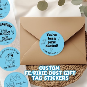 May include: A roll of light blue stickers with white text and illustrations, featuring phrases like "Pixie Dust" and "Bon Voyage!" A brown envelope rests on a woven basket. Text on the image reads "CUSTOM FE/PIXIE DUST GIFT TAG STICKERS."
