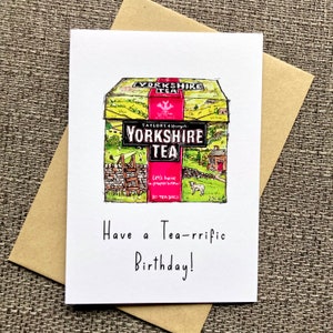May include: A birthday card featuring a hand-drawn illustration of a box of Yorkshire Tea. The box is yellow with green and brown accents and features a red logo with the text "Yorkshire Tea". The text "Have a Tea-rrific Birthday!" is written below the illustration.
