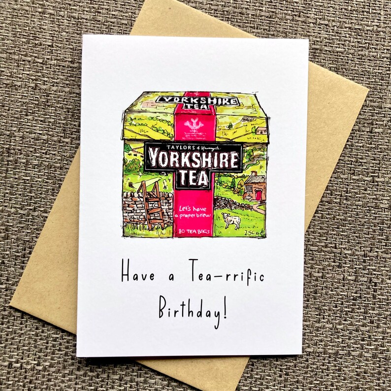 May include: A birthday card featuring a hand-drawn illustration of a box of Yorkshire Tea. The box is yellow with green and brown accents and features a red logo with the text "Yorkshire Tea". The text "Have a Tea-rrific Birthday!" is written below the illustration.