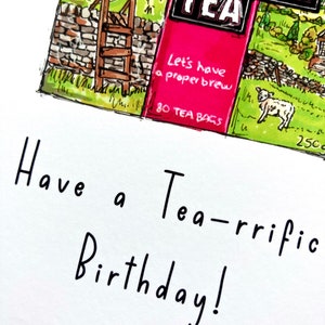 May include: A white card with black handwritten text that says "Have a Tea-rrific Birthday!"  The card has a small image of a tea box with a green and brown countryside scene and the words "Yorkshire Tea" in black and white. The tea box has a pink section with the words "Let's have a proper brew" and "80 Tea Bags" in white.