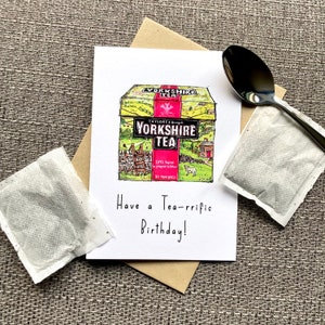 May include: A birthday card with a hand-drawn illustration of a box of Yorkshire Tea. The box is yellow with a red and white label. The text on the card reads "Have a Tea-rrific Birthday!"