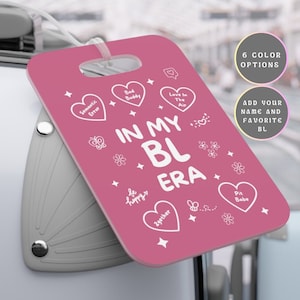 May include: Pink luggage tag with white text that says "In My BL Era" with hearts and other cute illustrations.  The tag has a hole at the top for a luggage strap.