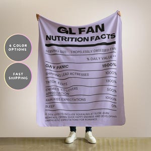 May include: A lilac blanket featuring the text "GL FAN NUTRITION FACTS" in black. The blanket lists "Gay Panic" at 1500% and "Sleep" at 0%. Includes "Side Effects" text. Two circles on the left say "6 COLOR OPTIONS" and "FAST SHIPPING".