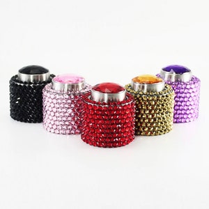 May include: Five bottle stoppers with a rhinestone design. The stoppers are black, pink, red, gold, and purple.