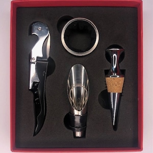 May include: A wine accessory set presented in a red box. The set contains a corkscrew, a wine pourer, a bottle stopper, and a drip ring. The tools are silver and black, with a black interior to the box.