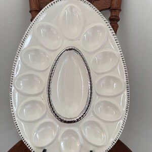 May include: White oval oyster serving platter with a silver-colored rope design around the center and a black and white dotted border. The platter has 12 oval indentations for oysters.