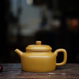 Könnte beinhalten: Eine gelbe Teekanne aus Keramik mit Deckel und Henkel. Die Teekanne steht auf einer Holzoberfläche.