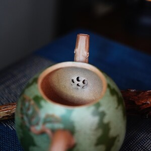 May include: A green and brown ceramic teapot with a wooden handle and a strainer with multiple holes in the lid.