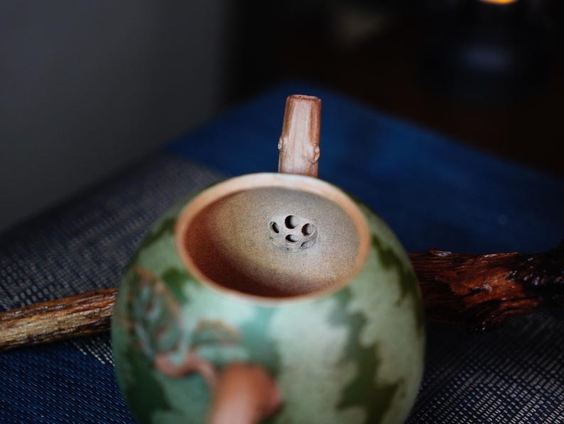 May include: A green and brown ceramic teapot with a wooden handle and a strainer with multiple holes in the lid.