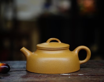 May include: A yellow ceramic teapot with a rounded body and a lid. The teapot has a small handle on the side and a spout on the front.