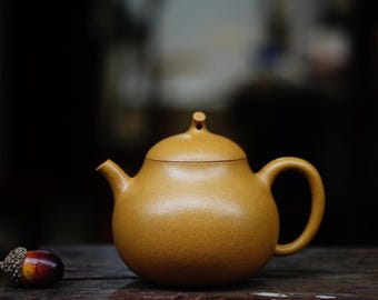 May include: A brown ceramic teapot with a rounded body and a small spout. The teapot is sitting on a wooden surface.