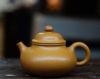 May include: A small, brown teapot with a lid and a handle. The teapot is made of ceramic and has a textured surface.