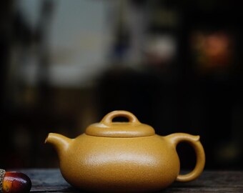 May include: A brown ceramic teapot with a rounded body and a lid. The teapot has a small handle on the side and a spout on the front.