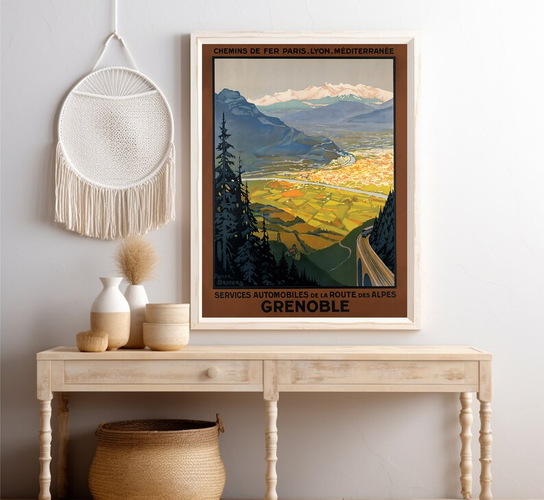 May include: Vintage travel poster advertising a trip to Grenoble, France. The poster features a scenic view of the French Alps with a winding road leading to the city. The text on the poster reads "Chemins de Fer Paris, Lyon, Mediterranee" and "Services Automobiles de la Route des Alpes Grenoble".