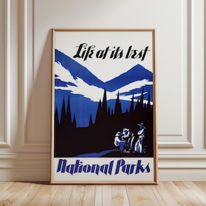 May include: A framed poster featuring a blue and white mountain landscape with a dark forest silhouette and three figures in the foreground. The text "Life at its best" appears at the top, and "National Parks" is printed in bold at the bottom.
