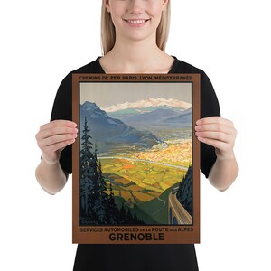 May include: A vintage travel poster advertising a train journey to Grenoble, France. The poster features a scenic view of the French Alps with a winding road leading to the city of Grenoble. The text on the poster reads "Chemins de Fer Paris. Lyon. Mediterranee" and "Services Automobiles de la Route des Alpes Grenoble".