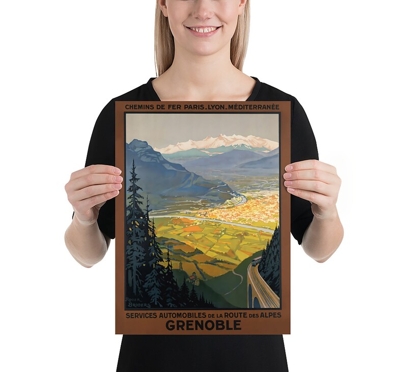 May include: A vintage travel poster advertising a train journey to Grenoble, France. The poster features a scenic view of the French Alps with a winding road leading to the city of Grenoble. The text on the poster reads "Chemins de Fer Paris. Lyon. Mediterranee" and "Services Automobiles de la Route des Alpes Grenoble".
