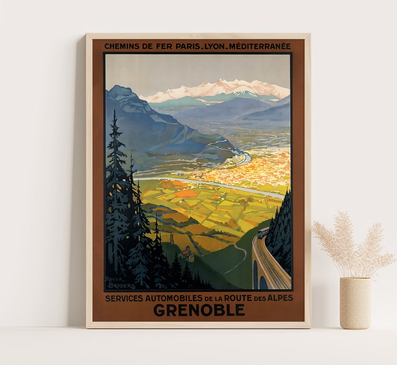 May include: A vintage travel poster advertising train and automobile services to Grenoble, France. The poster features a scenic view of the city nestled in the French Alps with snow-capped mountains in the background. The text reads "Chemins de Fer Paris-Lyon-Mediterranee Services Automobiles de la Route des Alpes Grenoble".